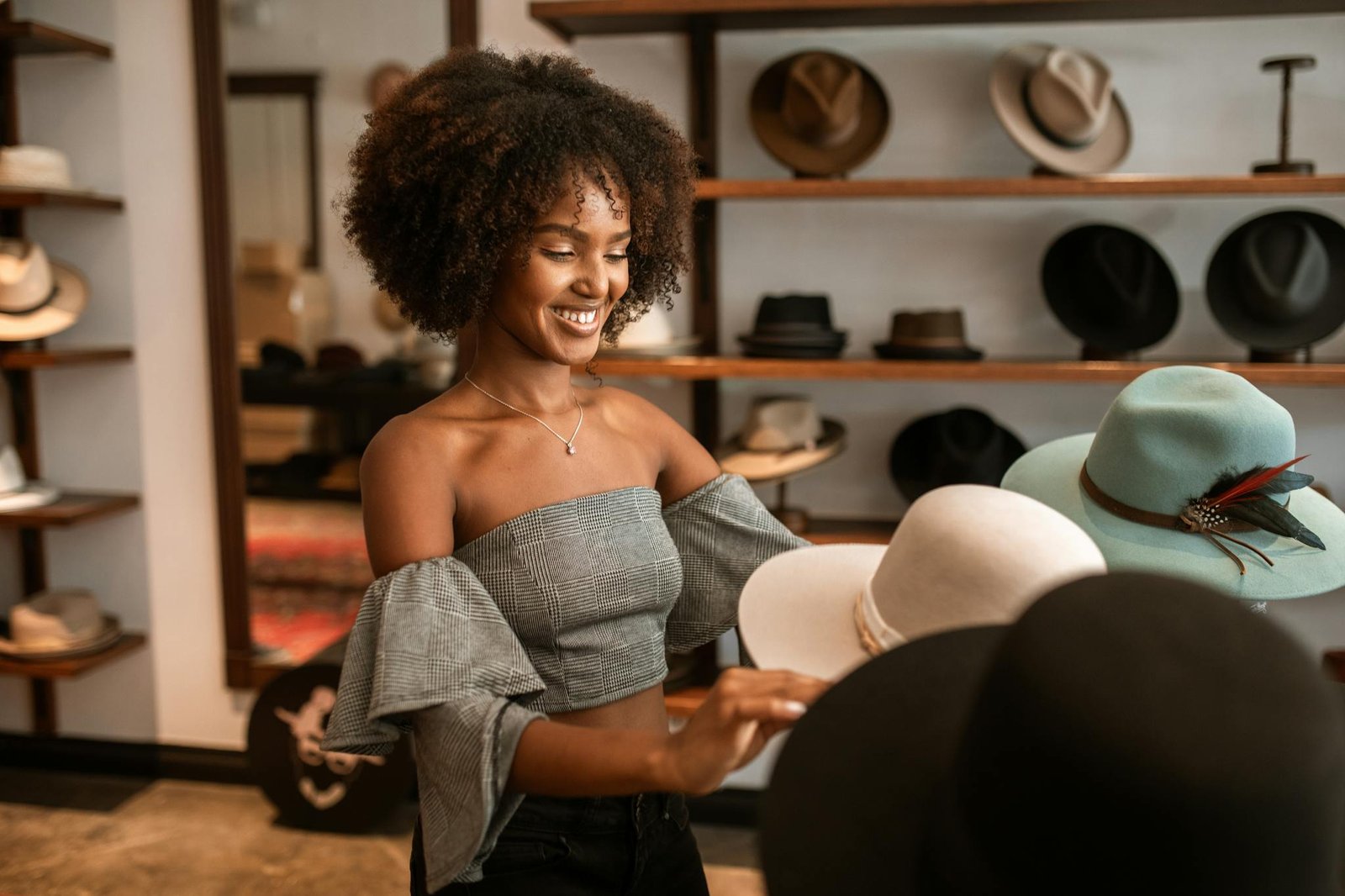 A joyful woman with curly hair exploring various hats in a stylish boutique.