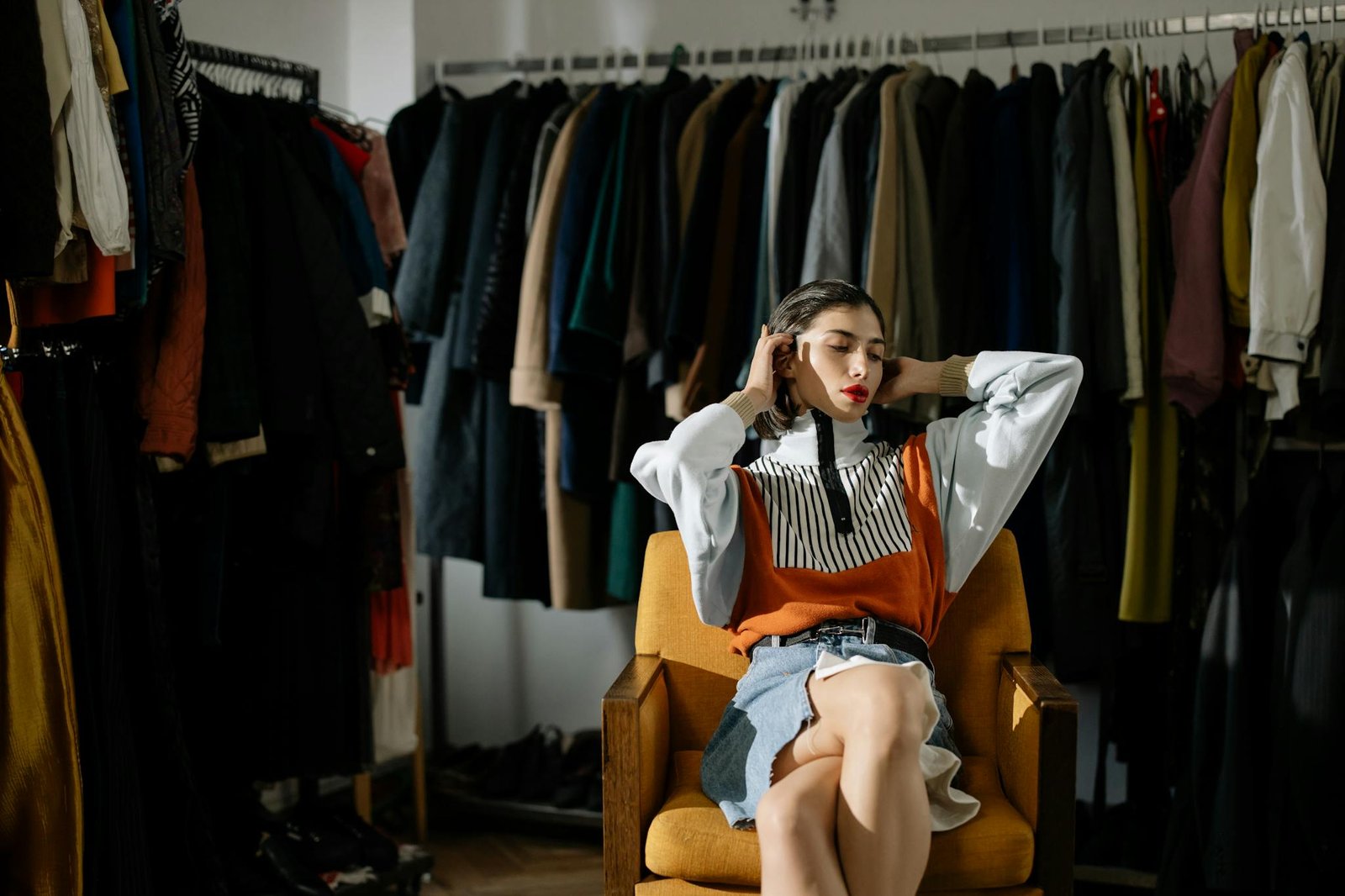 A stylish female model sits in a retro wardrobe setup.